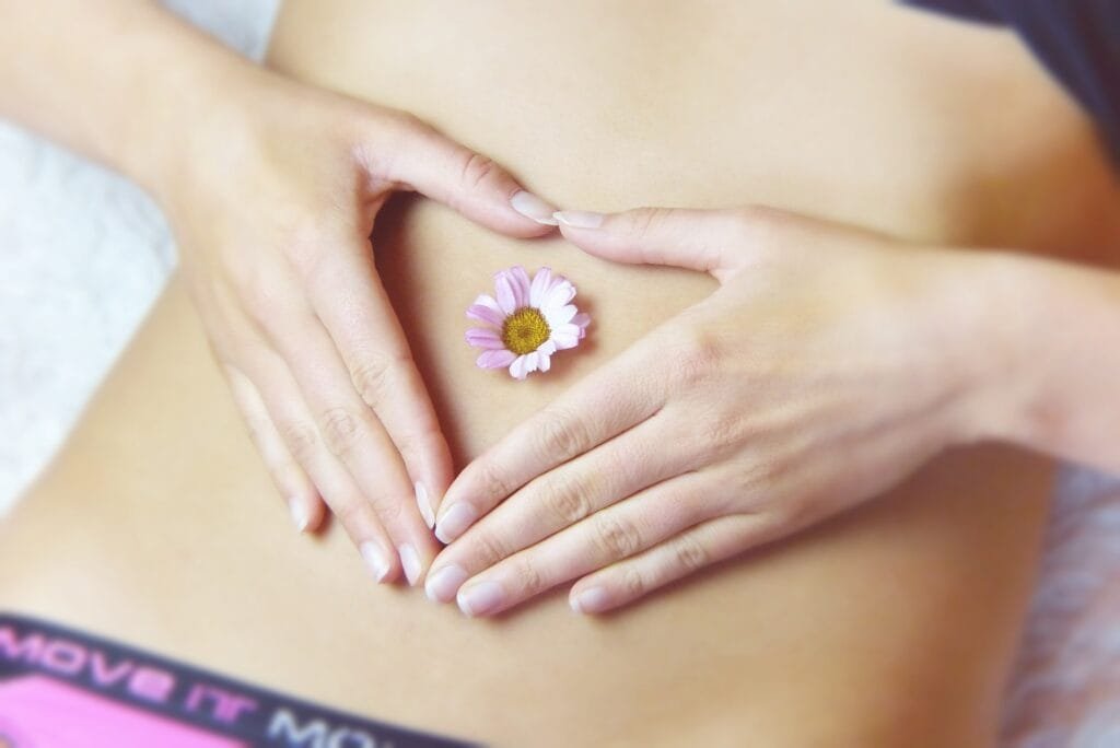 A heart shape with their hands over their belly, with a flower placed in the center.