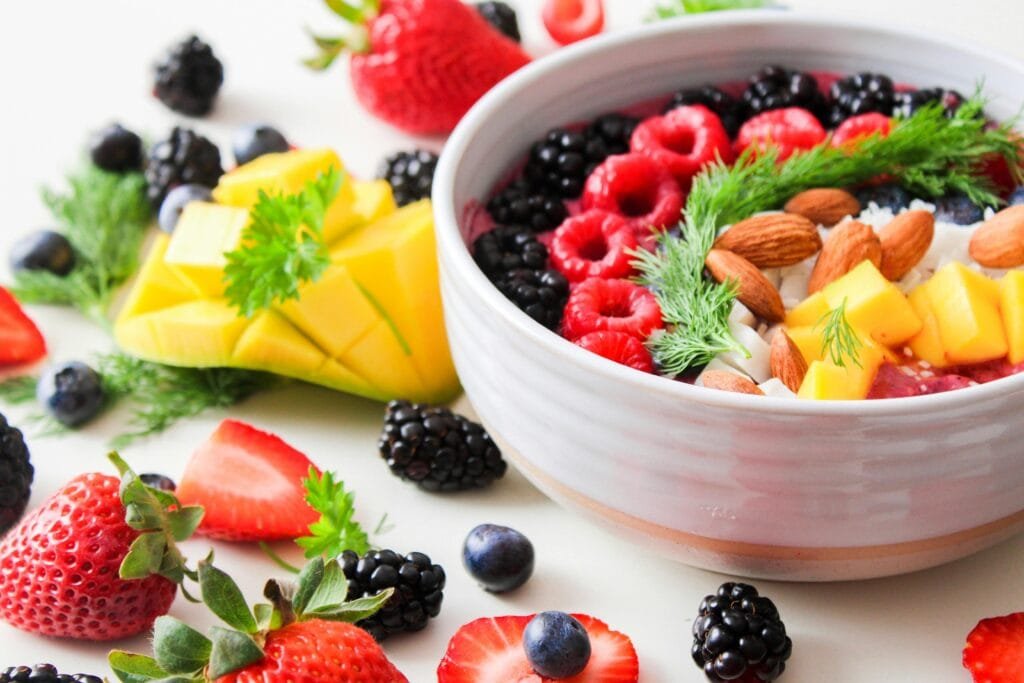A bowl filled with various fruits like berries and mango, topped with almonds and coconut flakes.