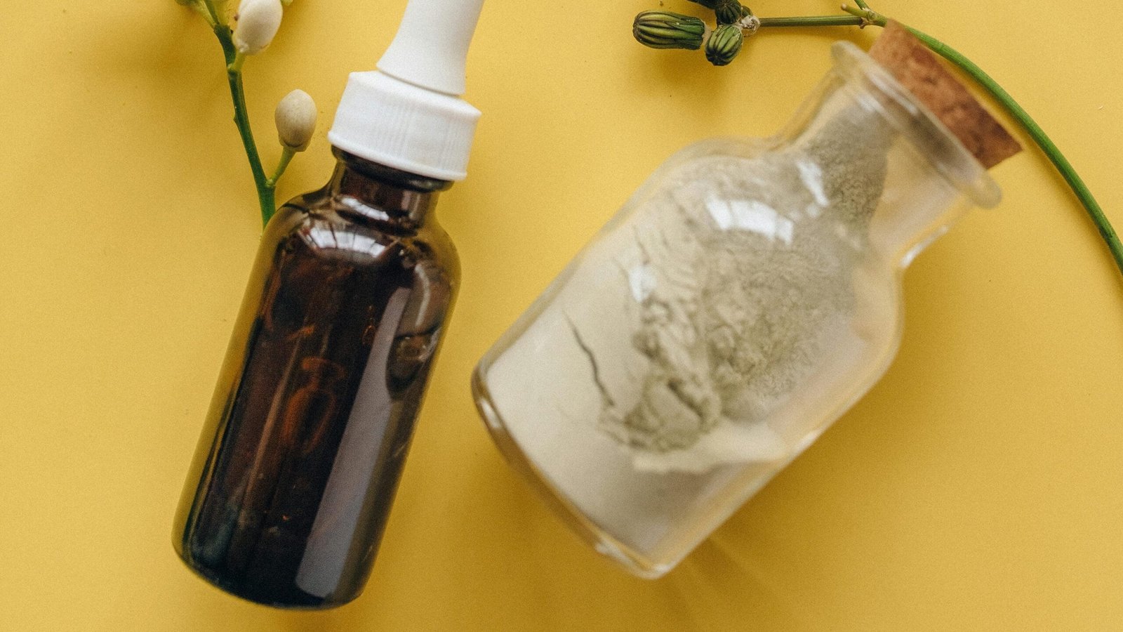 A yellow surface with two brown bottles, one containing a white powder, and a nasal spray bottle, along with some plants.