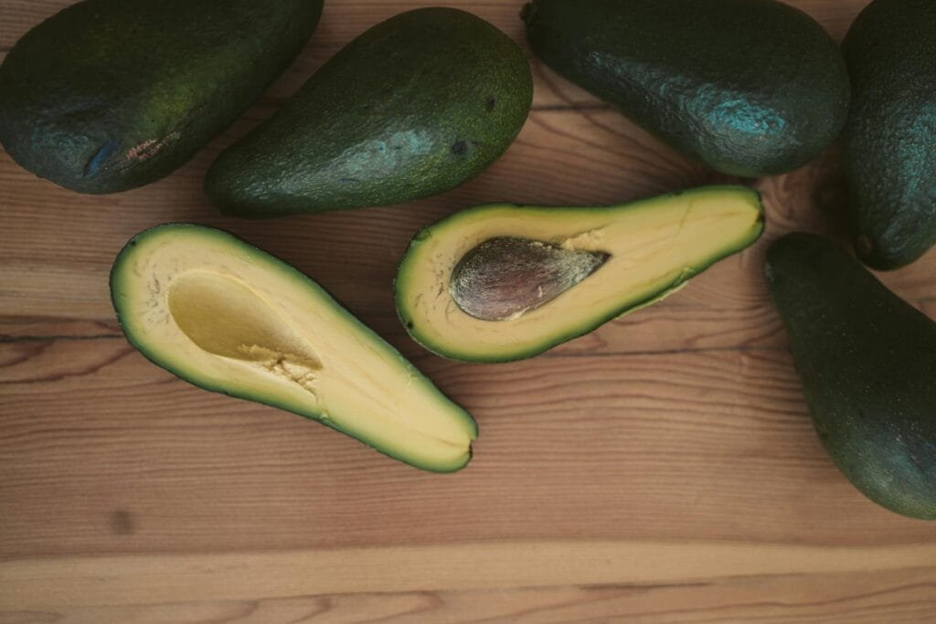 The picture shows avocados, with one of them cut in half, revealing the flesh and the large seed inside