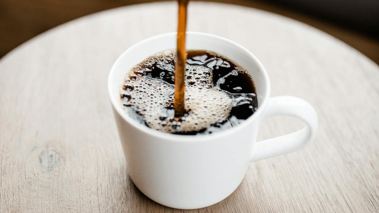 A cup of coffee being filled from a carafe.