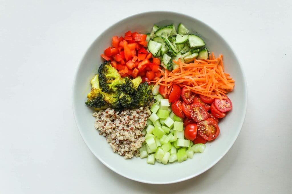 A bowl of quinoa salad with various vegetables, including cherry tomatoes, cucumber, broccoli, bell peppers, and carrots.
