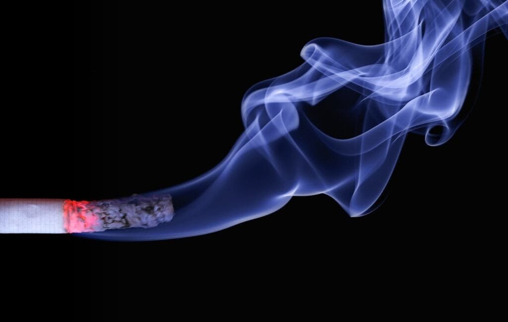 A lit cigarette with smoke rising from it against a black background.