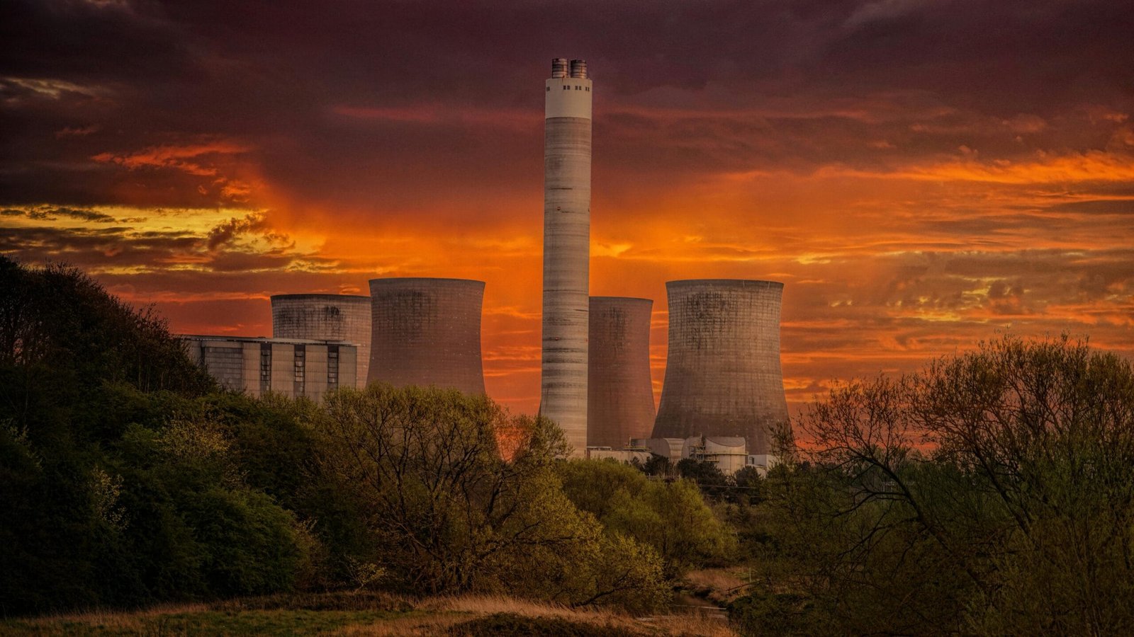 A nuclear power plant with a vibrant orange and yellow sky at sunset.